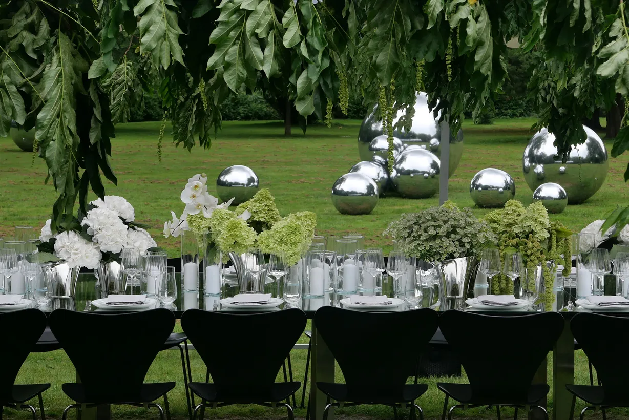 Langt festbord med hvide blomster og sorte stole i en park med spejlkugler, sat op til bryllup på Glorup Gods