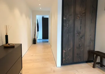 Entré med lyst plankegulv og en høj garderobe med låger i mørkt, groft træ