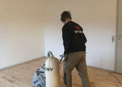Gulvsliber fra Nemovo med høreværn sliber et parketgulv med en båndslibemaskine