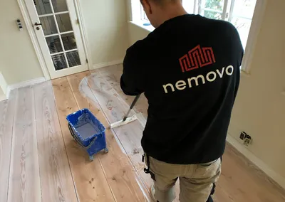 Medarbejder fra Nemovo påfører overfladebehandling på et nyslebet plankegulv med en moppe