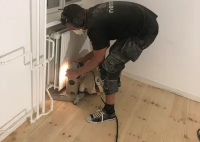 Gulvsliber fra Nemovo sliber et fyrregulv helt ind under en radiator med en kantsliber