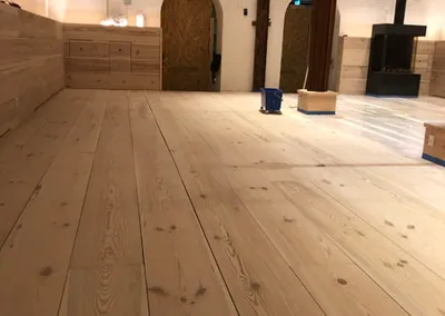 Nylagt gulv af brede, lyse træplanker i en stor sal med hvide murstensvægge og buede døråbninger