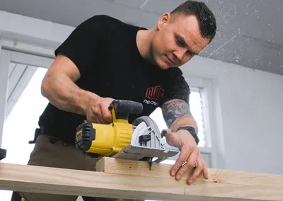 Tømrer fra Nemovo skærer et bræt til med rundsav i et lyst rum under renovering