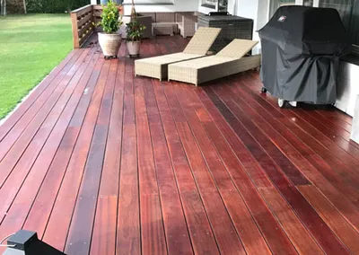 Nyoliet terrasse i rødbrunt hårdttræ med liggestole og grill under en markise