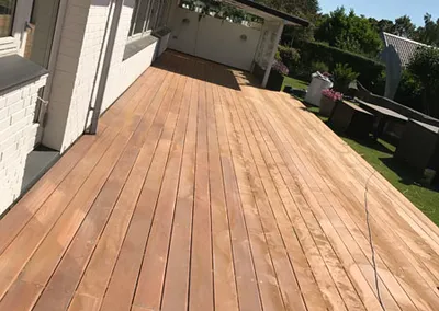 Lang træterrasse langs et hvidt hus, lys og ubehandlet før oliering