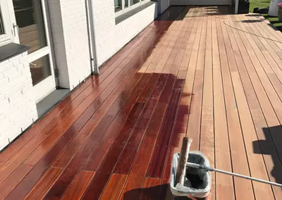 Træterrasse under oliering: den ene halvdel er mørk af olie, og der står en spand og en rulle ved siden af