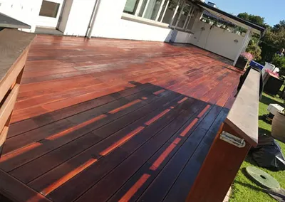 Færdigoliet terrasse i rødbrunt hårdttræ langs et hvidt hus i aftensol