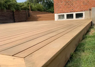 Ny terrasse i lyst hårdttræ med pæn kantafslutning ved et rødt murstenshus