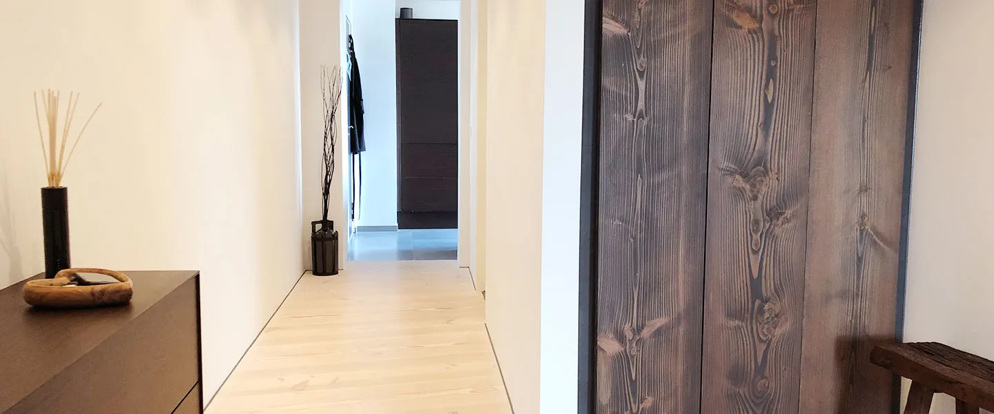 Renoveret gang med lyse plankegulve, hvide vægge og døre i mørkt træ