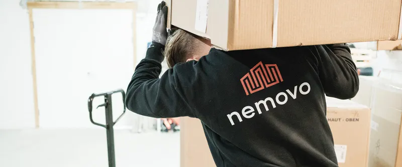 Flyttemand fra Nemovo bærer en stor papkasse på skuldrene på et lager