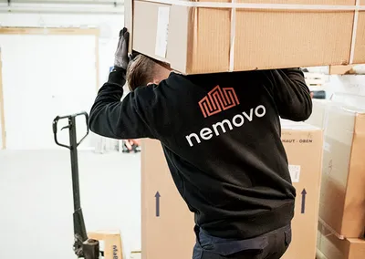Flyttemand fra Nemovo bærer en stor papkasse på skuldrene på et lager