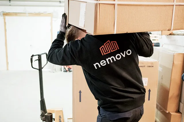 Flyttemand fra Nemovo bærer en stor papkasse på skuldrene på et lager