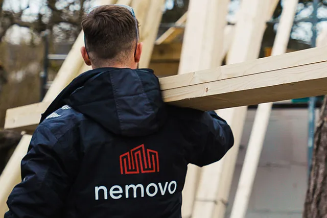 Tømrer fra Nemovo bærer planker på skulderen på en byggeplads