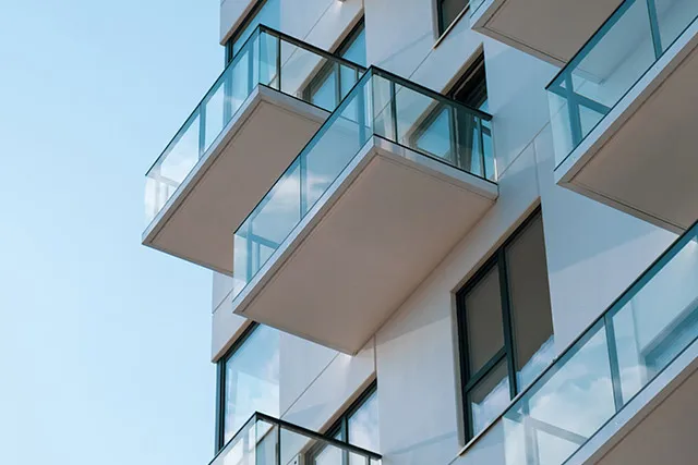 Hvid boligblok med altaner med glasværn mod en blå himmel