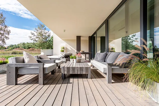 Overdækket træterrasse med loungemøbler foran et moderne hus